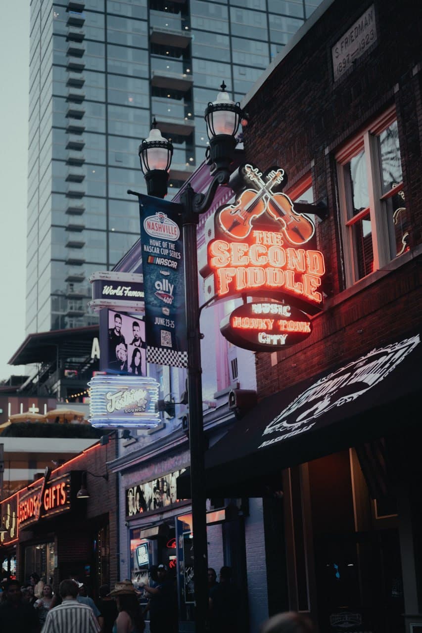 Downtown Nashville honky-tonk street scene at dusk with neon signs for The Second Fiddle and Johnny Cash's
